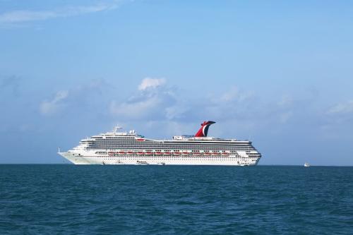 The Carnival Conquest cruise ship cruises through calm blue ocean waters with a small boat nearby.