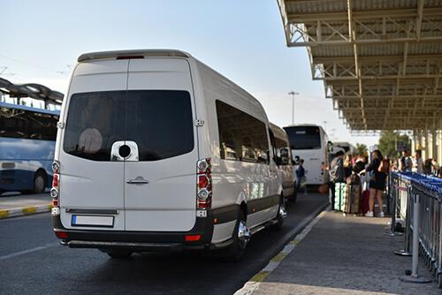 A white shuttle van waits at a terminal loading zone, ready to transport passengers and luggage to the cruise port.