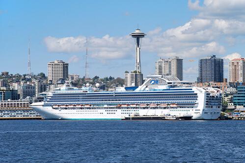 A Princess Cruises ship docked in Seattle with the Space Needle and downtown skyline in the background.