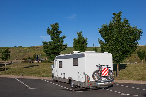 A motorhome with bikes mounted on the back parked in a grassy lot, representing RV and oversized vehicle parking.