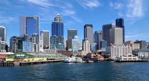 The Seattle downtown skyline and historic waterfront piers viewed from the water on a clear, sunny day.