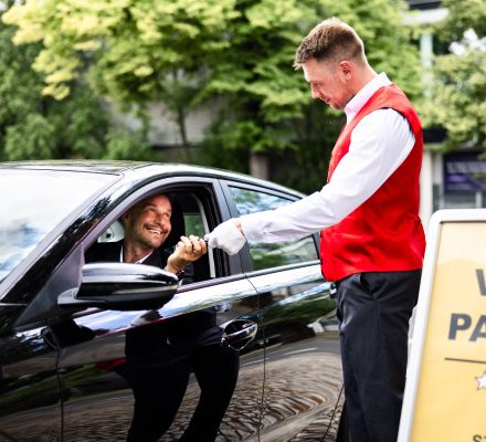 Driver handing keys to a valet attendant in a black car.